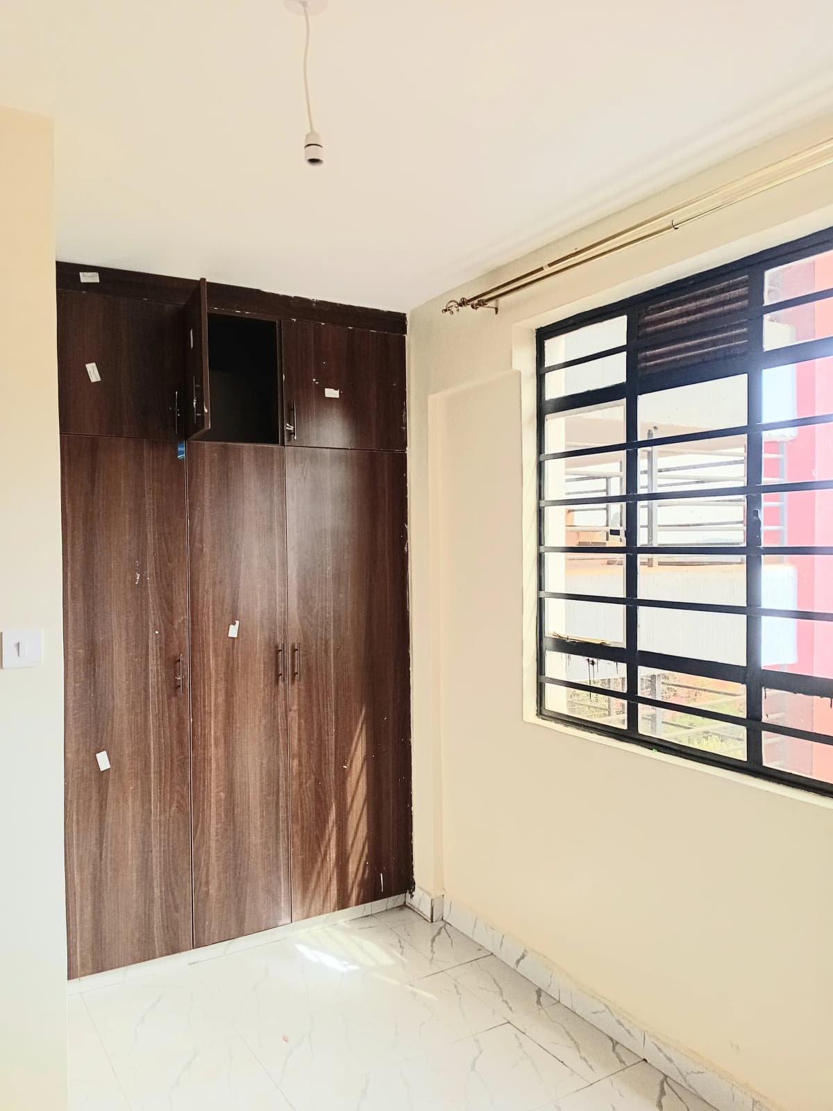 Unfurnished bedroom with wooden wardrobe and barred window