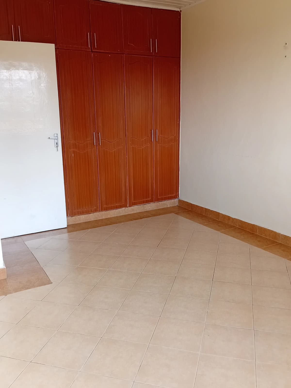 Spacious bedroom with wooden built-in wardrobe and tile flooring