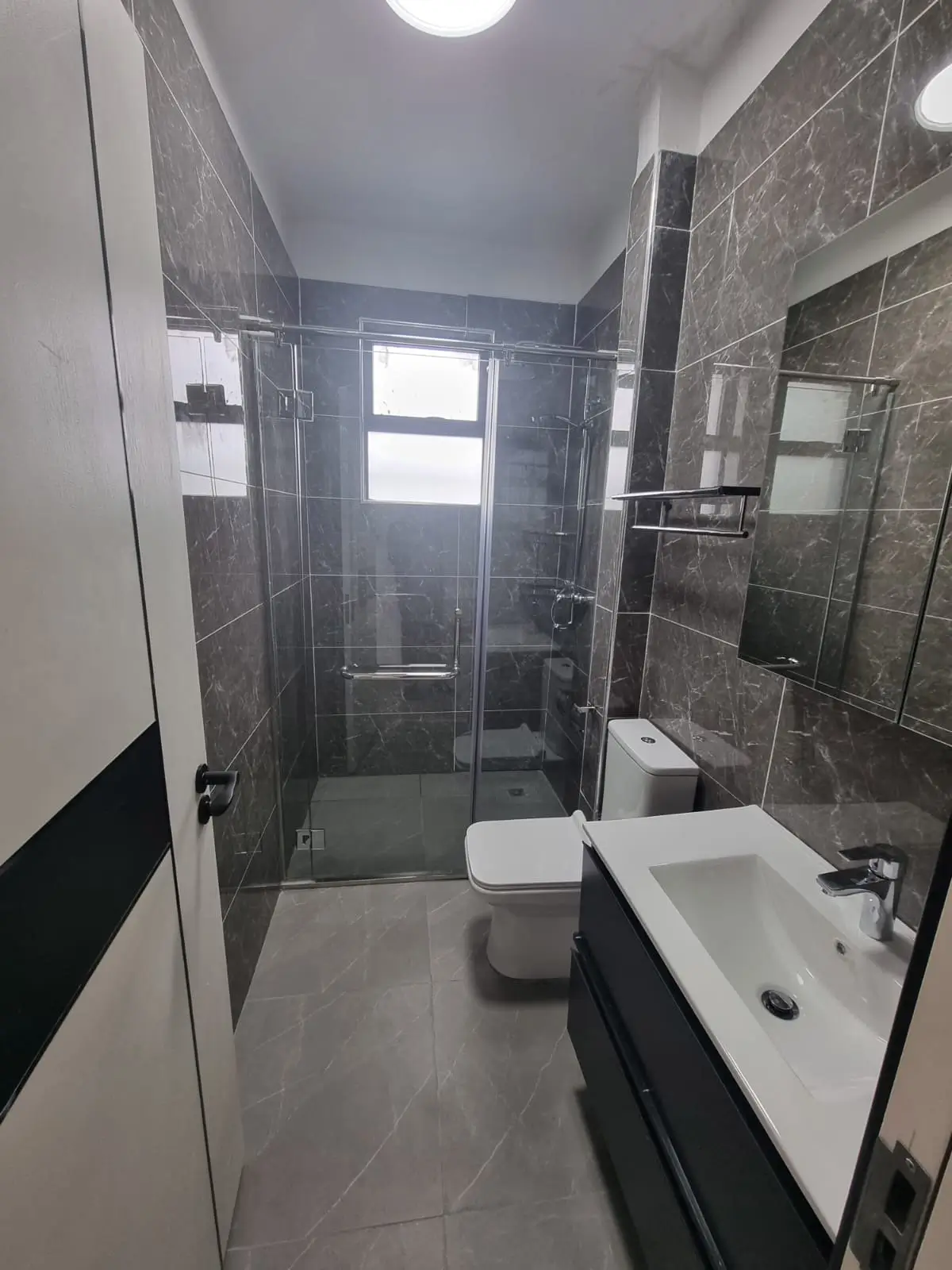 Modern bathroom with dark marble tiles, glass shower enclosure