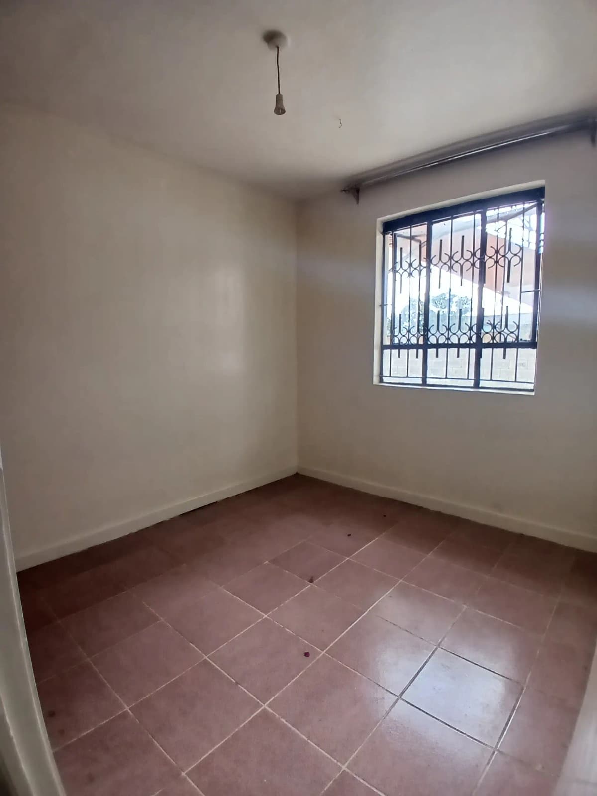 Empty bedroom with terracotta tiles and barred window