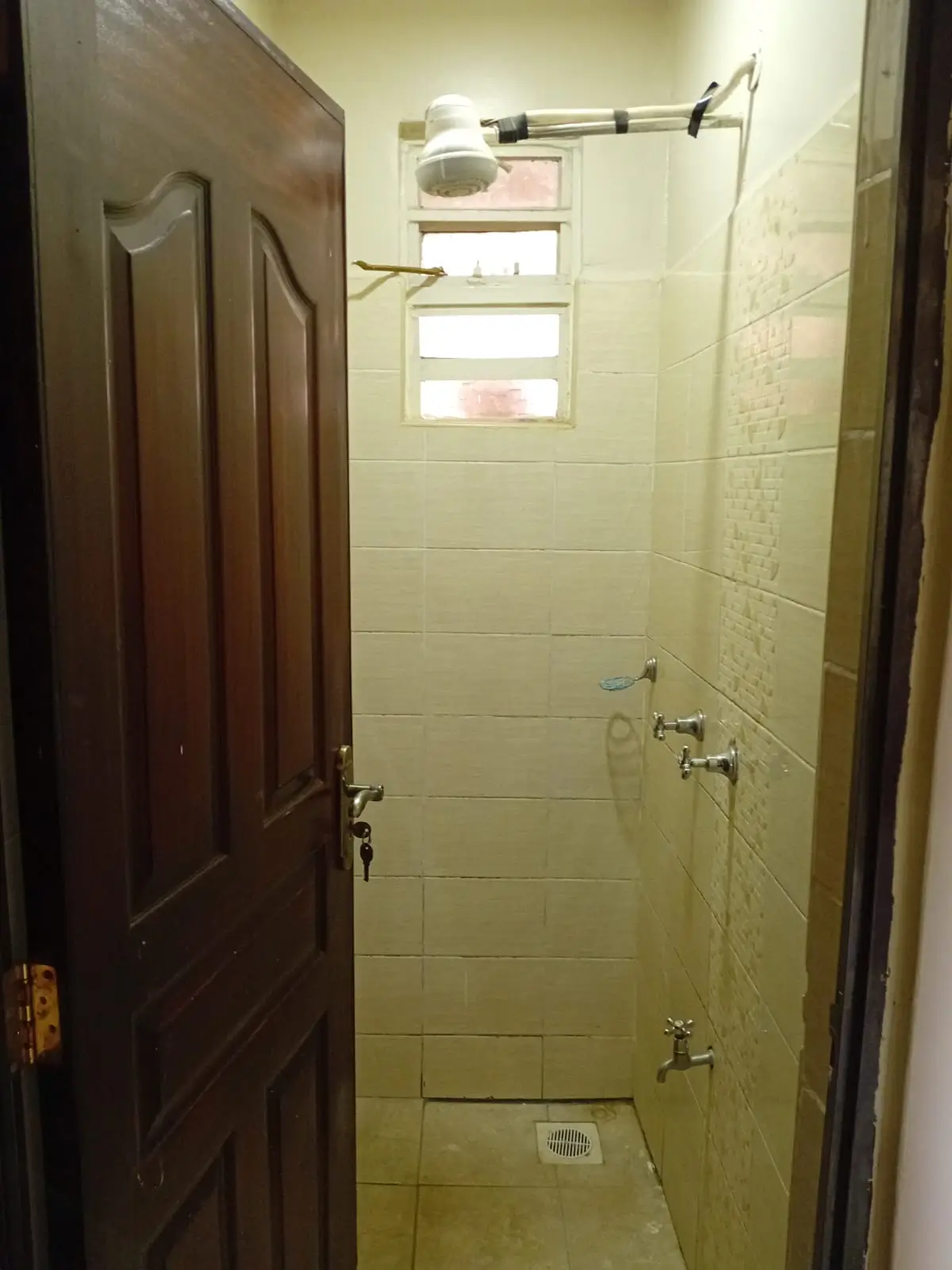 Basic bathroom with cream tiles, shower area, wooden door