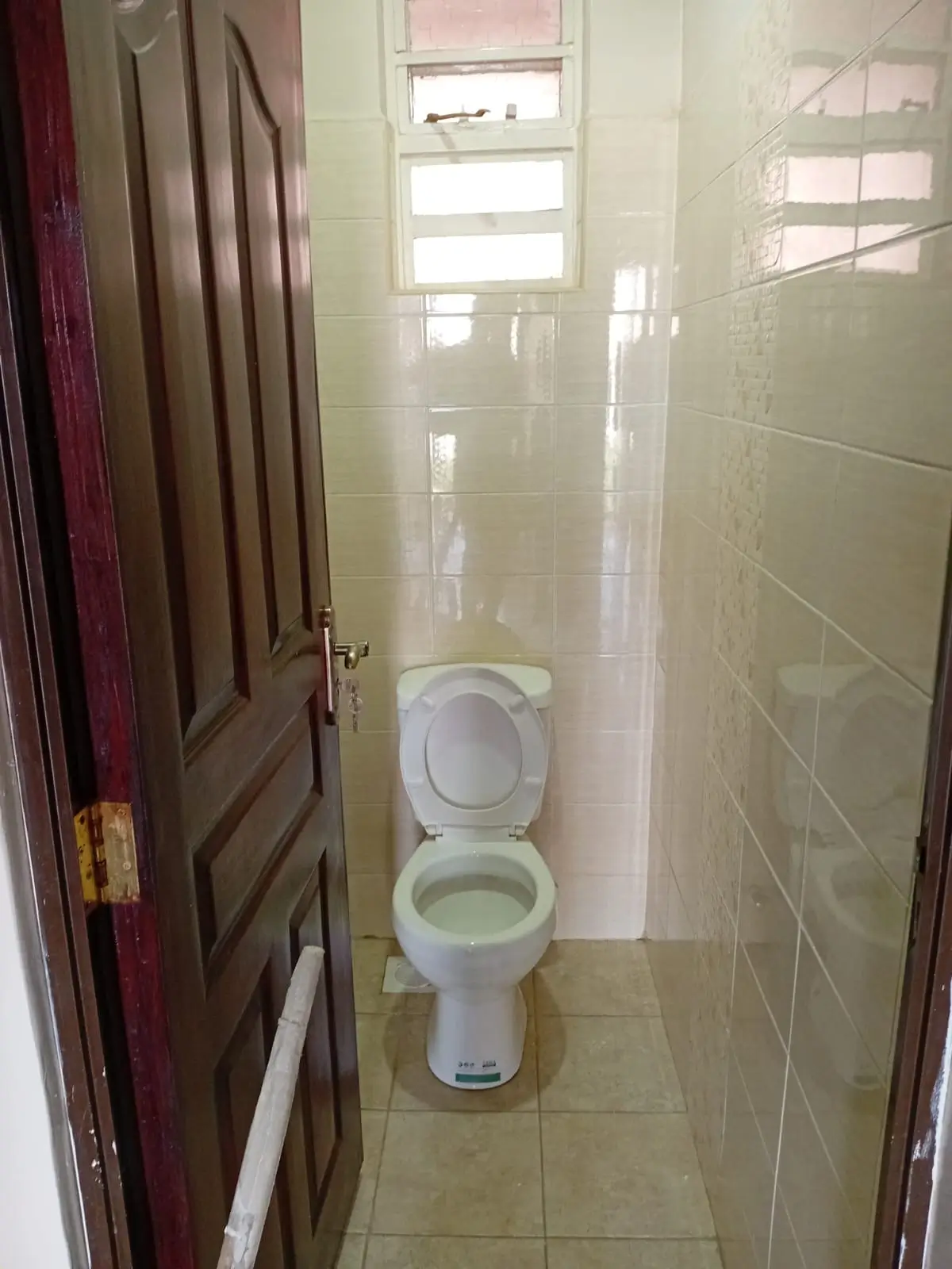 Narrow bathroom with toilet, tiled walls and window.