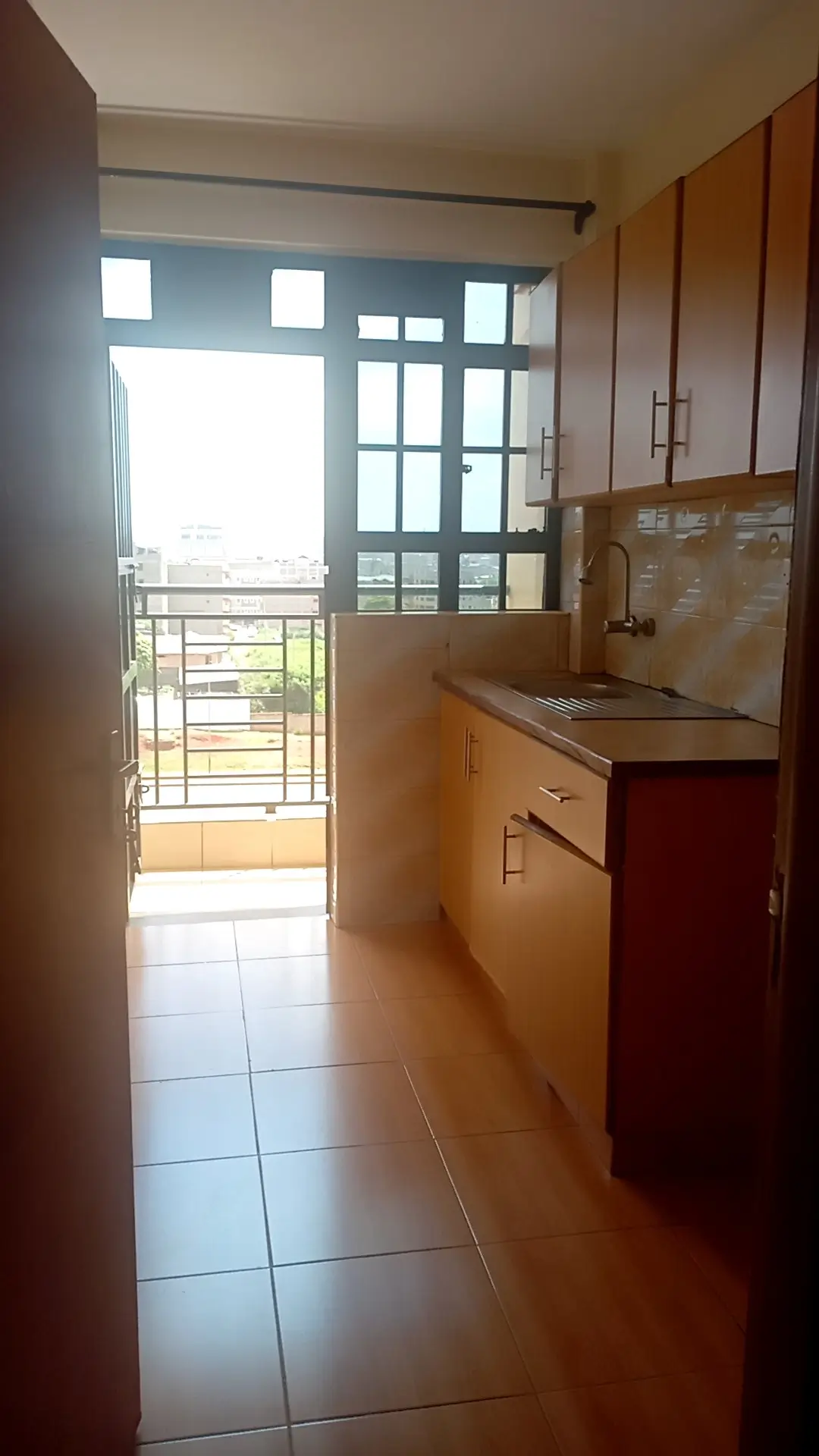 Compact kitchen with wooden cabinets, balcony view beyond