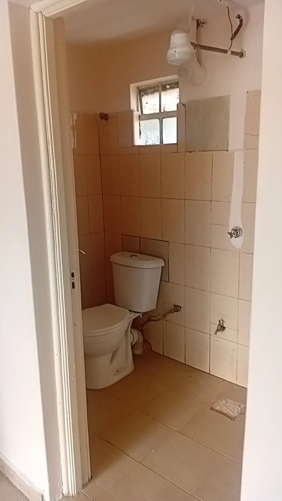 Compact bathroom with toilet, tile walls, and small window
